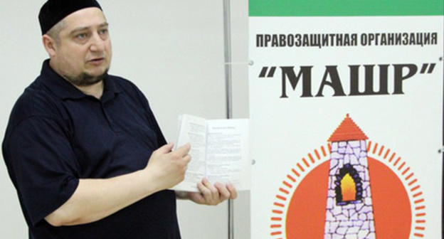 Magomed Mutsolgov near the poster with the "Mashr" logo. Photo http://mchenrycitizenstaxwatch.org/blogs/342/posts/28890