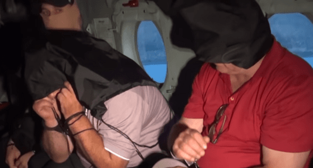 The detained suspects with bags over their heads in a helicopter. Screenshot of a video https://www.youtube.com/watch?v=2GZg1Npp3ds